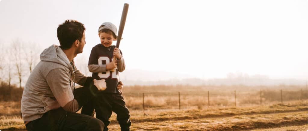 A father and son with a baseball bat in a field, from the All Pro Dad website